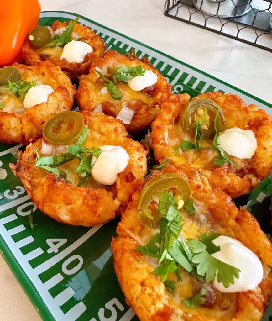 Chili Tater Tot cups with garnishes on football platter for game day snacks.