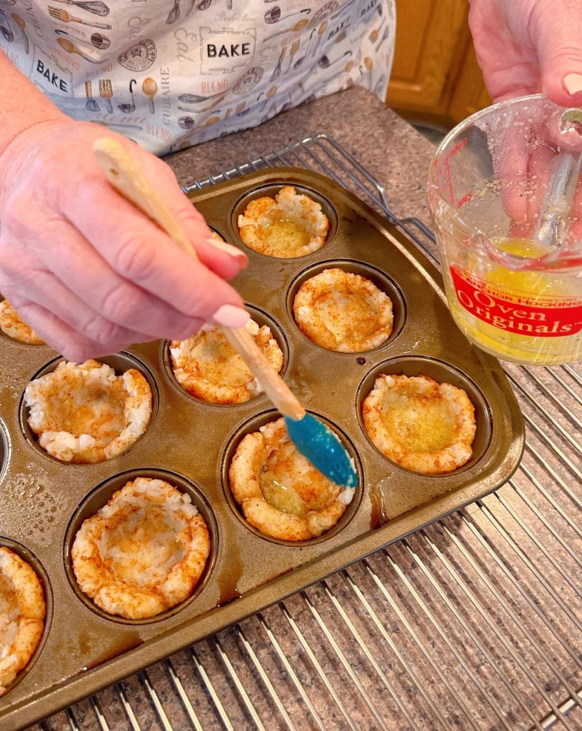 Brusing tater tot cups with garlic butter before baking.