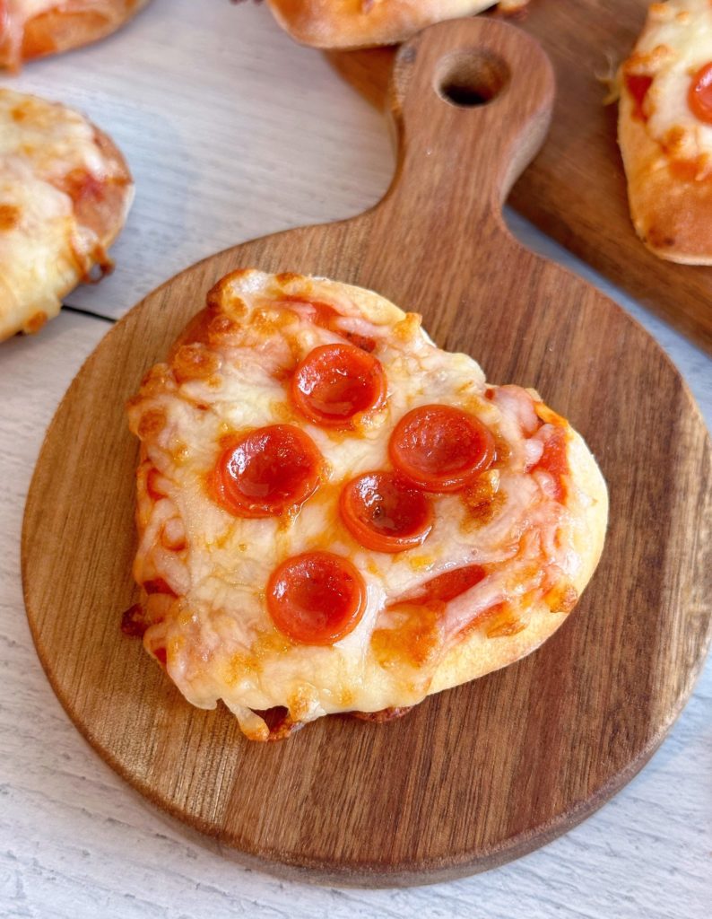 Close-up photo of a mini air fryer pepperoni pizza on a small cutting board.