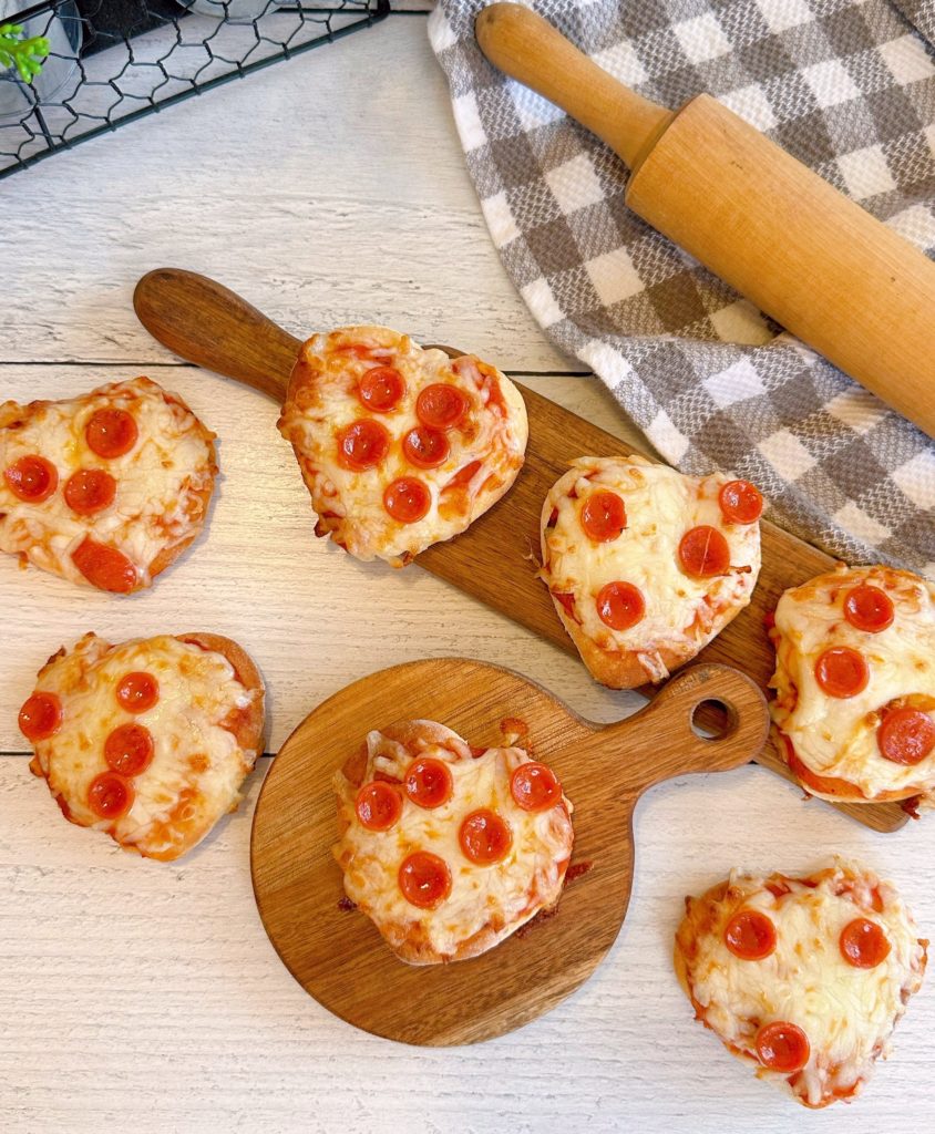 Mini heart shaped air fryer pizzas on small cutting boards.