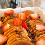 Breakfast casserole with syrup being poured over the top of it.