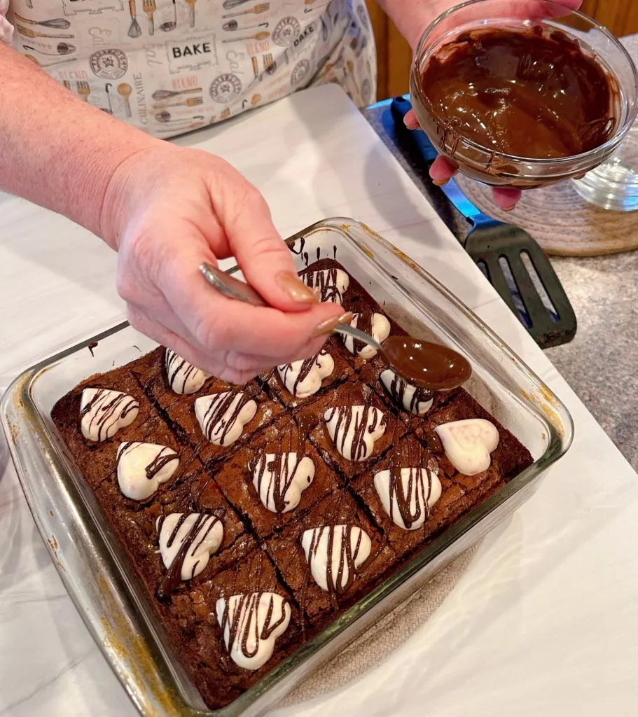 Drizzling melted chocolate over top of each brownie squar.