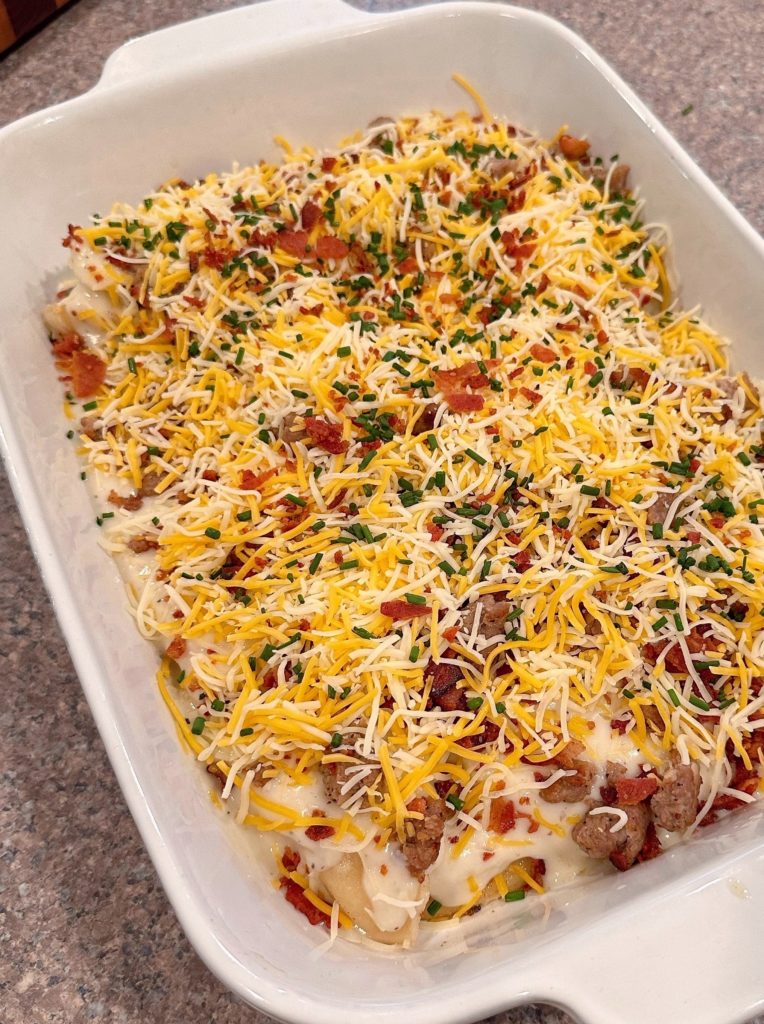 Pierogies Casserole topped with cheese and chives and ready to bake.