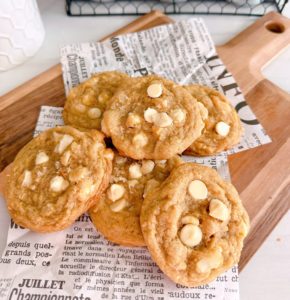 White Chocolate Chip Macadamia Nut cookies in a pile on a cutting board with news paper print.