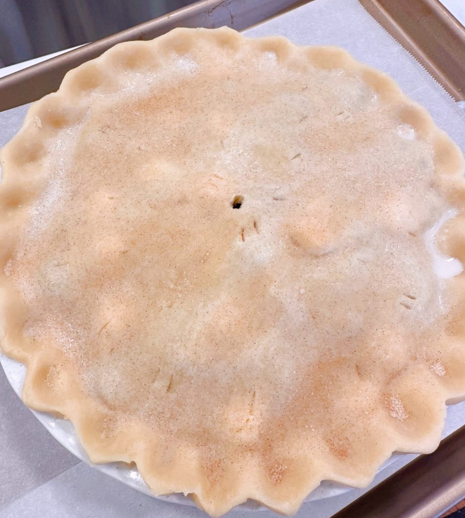 Pie on lined baking sheet sprinkled with cinnamon sugar ready to bake.