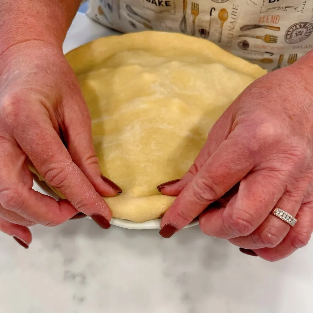 Sealing and crimping the top of the pie crust.