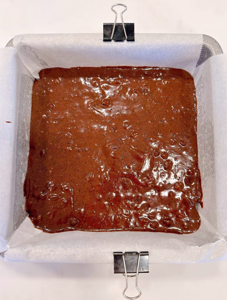 Brownie batter in prepared baking pan with parchment paper.