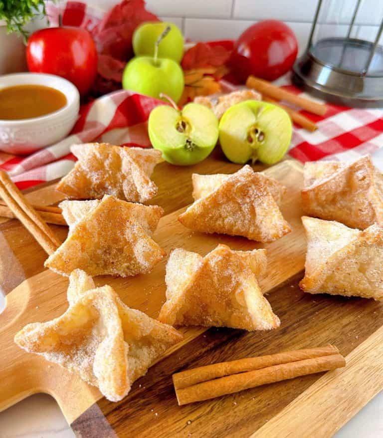 Apple Pie Bites on a wooden cutting board with apples, caramel, and cinnamon sticks.