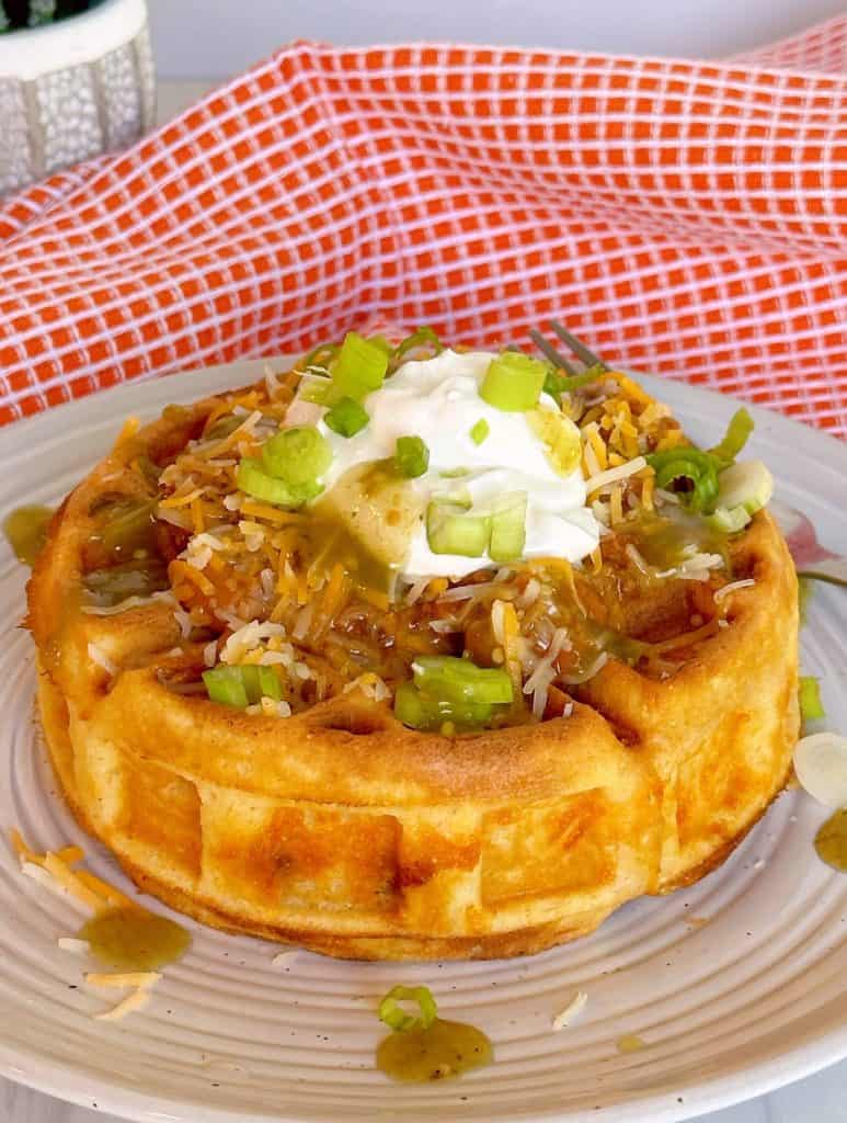 Cornbread waffle stuffed with chili and cheese and topped with sour cream and more cheese on a dinner plate.