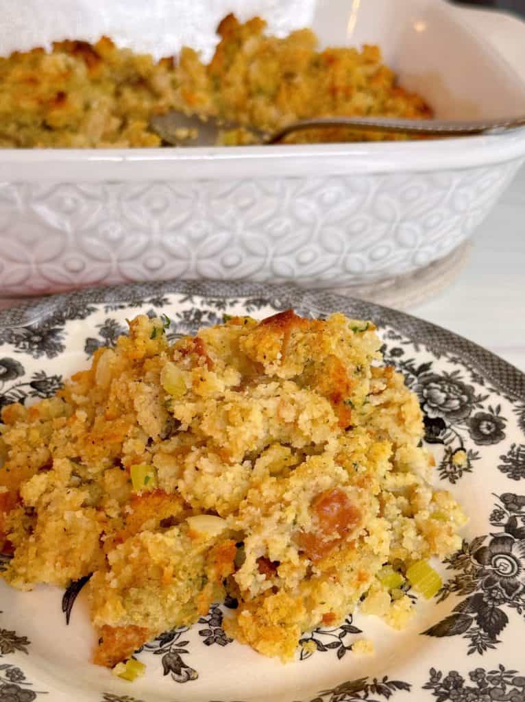 Cornbread dressing on a serving plate with casserole dish in the background.