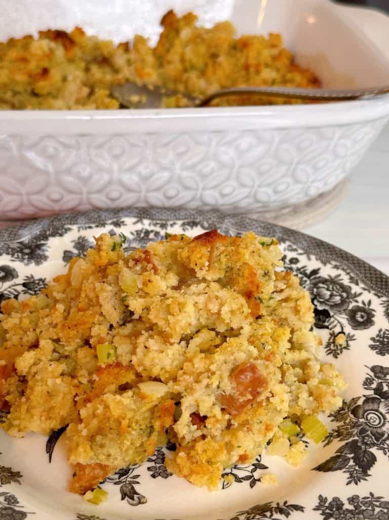 Cornbread dressing on a serving plate with casserole dish in the background.