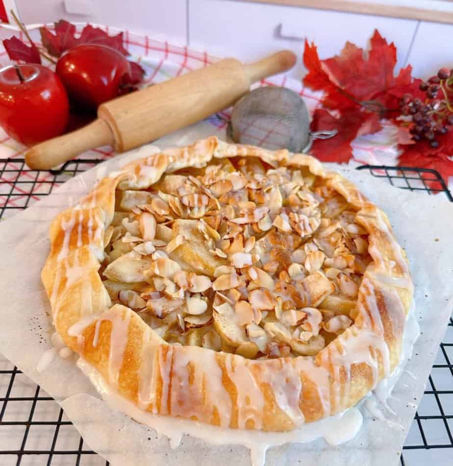 Apple Almon Galette on a cooling rack with a rolling pin and apples in the back ground.