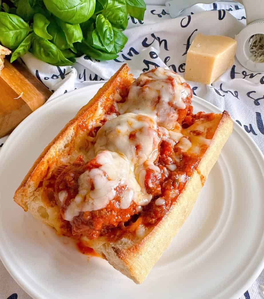Meatball sub sandwich on a white plate with toasted bread and melted cheese.