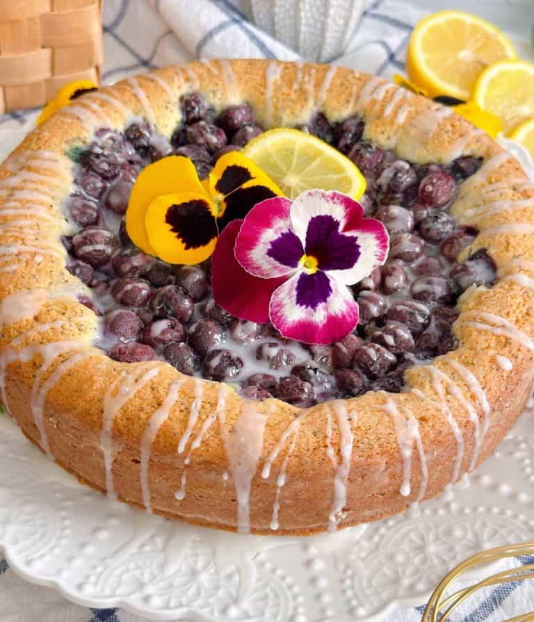 Blueberry Lemon Poppy seed cake with pansies and lemon glaze on a cake plate.