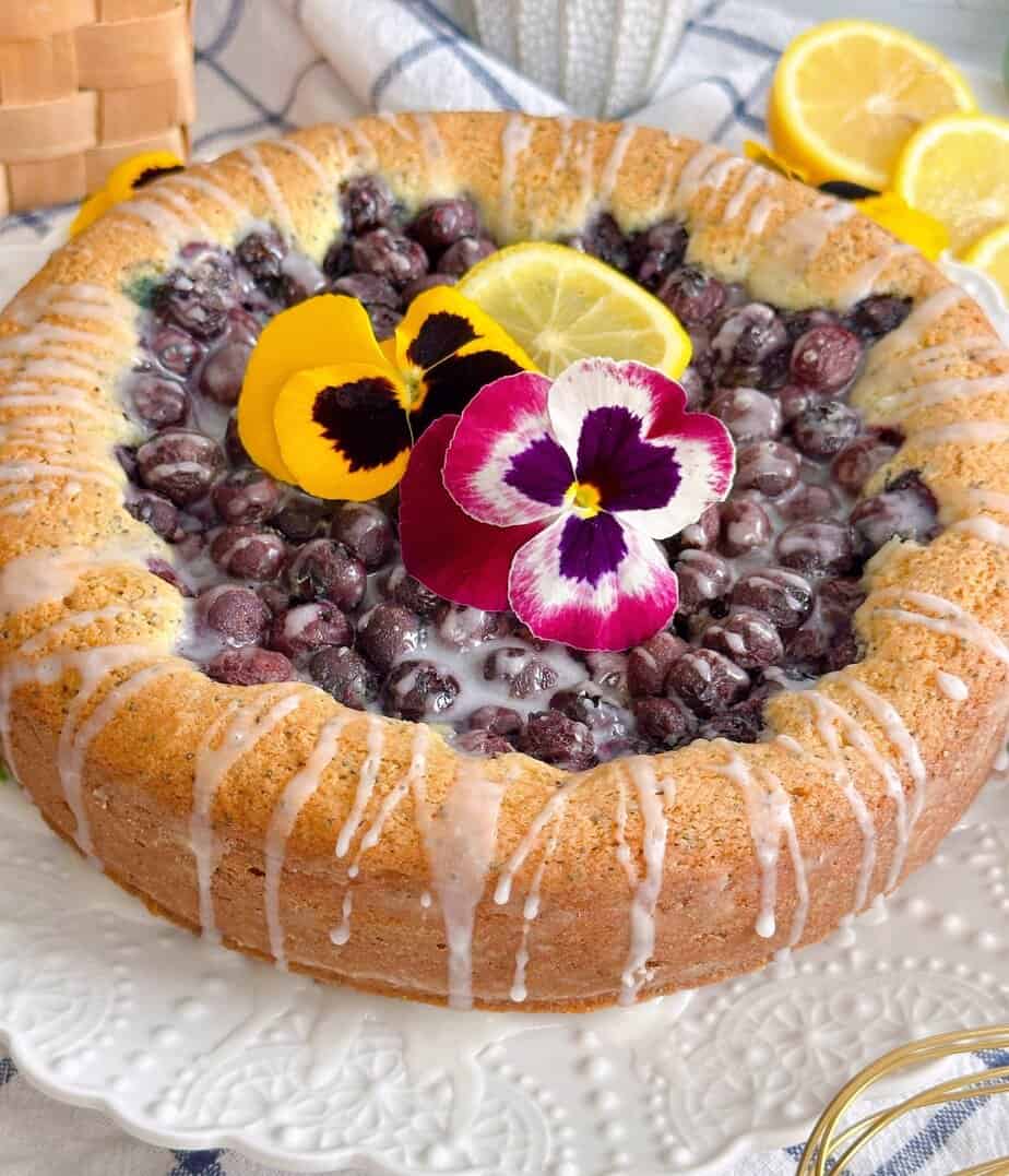 Blueberry Lemon Poppy seed cake with pansies and lemon glaze on a cake plate.