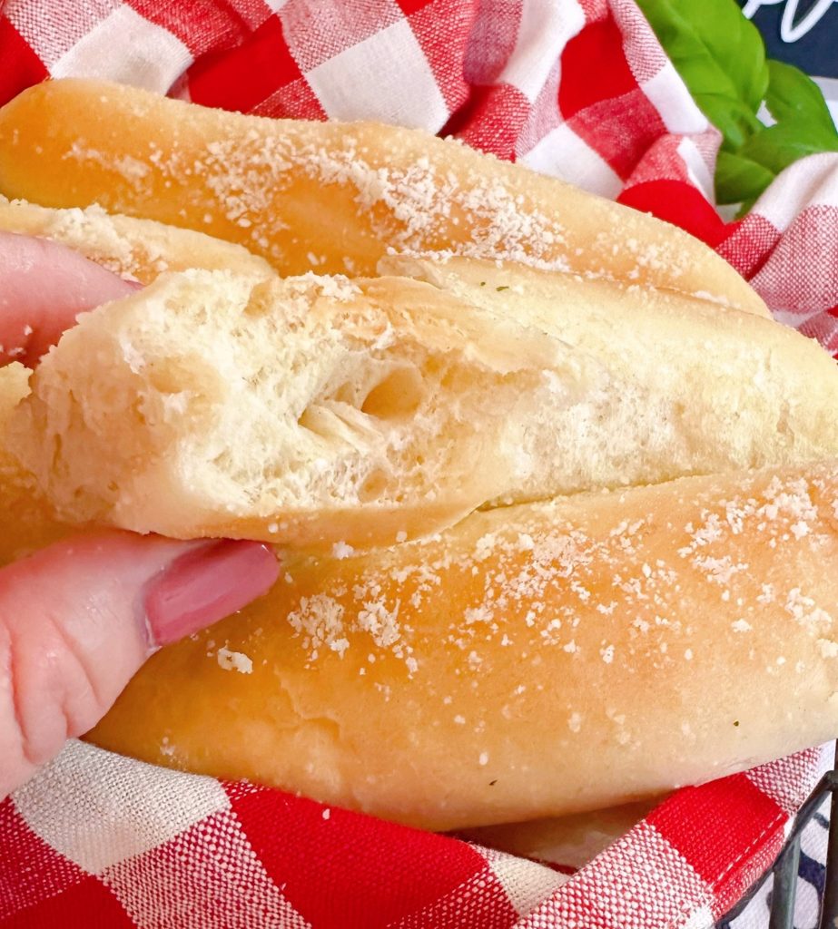 Breadstick is held in bakers hand with a bite out of it.