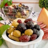Marinated Olives in a bowl on a cheese board with a bigger bowl of olives in the background.