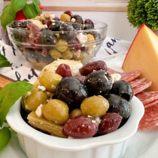 Marinated Olives in a bowl on a cheese board with a bigger bowl of olives in the background.