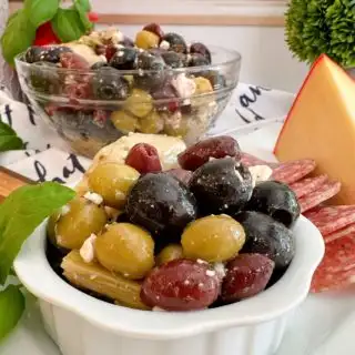 Marinated Olives in a bowl on a cheese board with a bigger bowl of olives in the background.