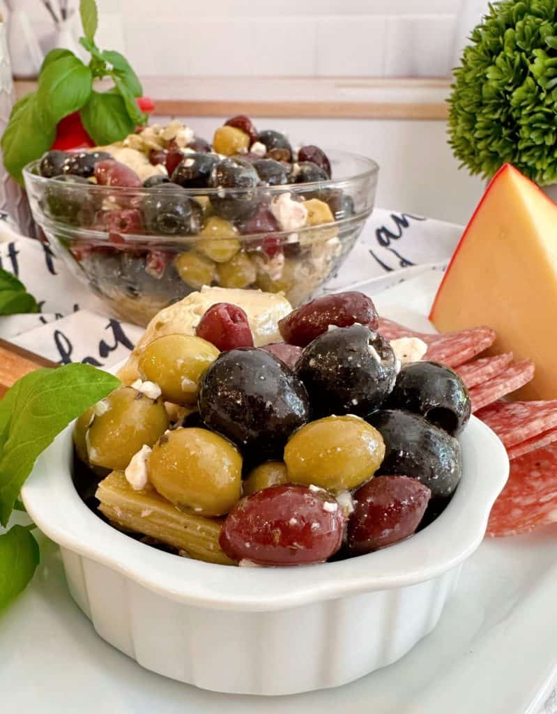 Marinated Olives in a bowl on a cheese board with a bigger bowl of olives in the background.