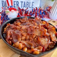 Baked Beans up-close in a small skillet on top of a cutting board.