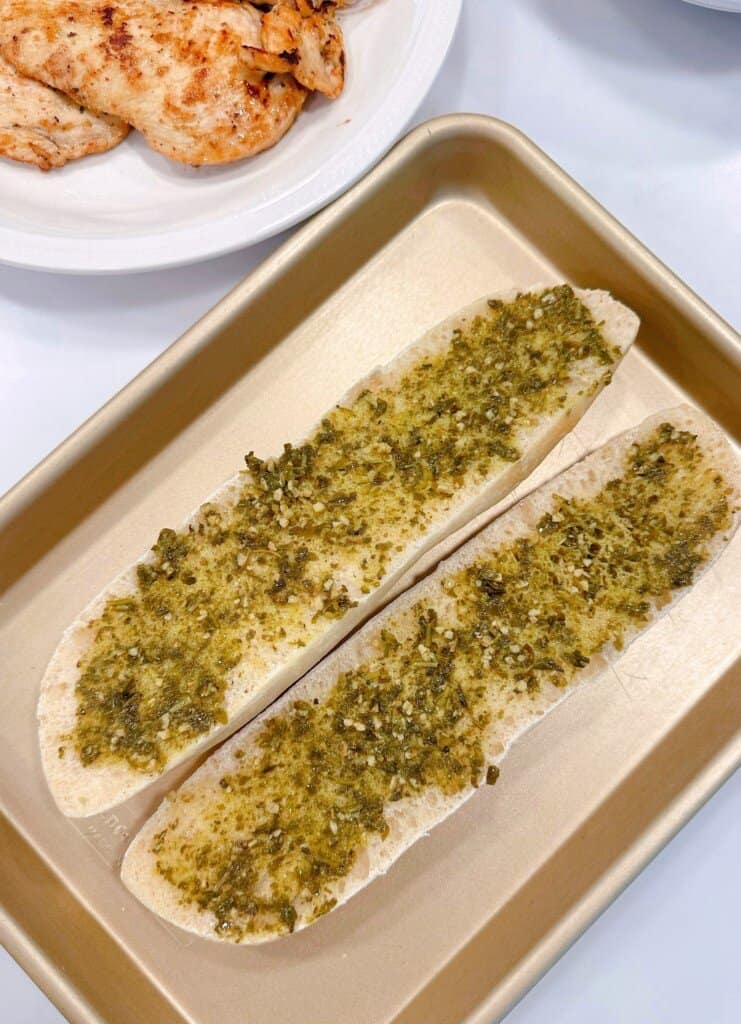 Each baguette is sliced in half and spread with pesto sauce.
