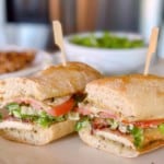 Chicken Cesar Sandwich with grilled chicken, lettuce, tomato, bacon. Cut in half on a baguette.
