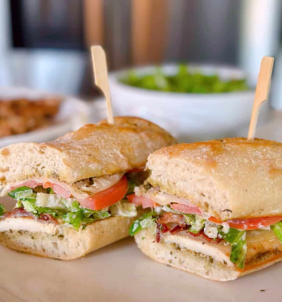 Chicken Cesar Sandwich with grilled chicken, lettuce, tomato, bacon. Cut in half on a baguette.