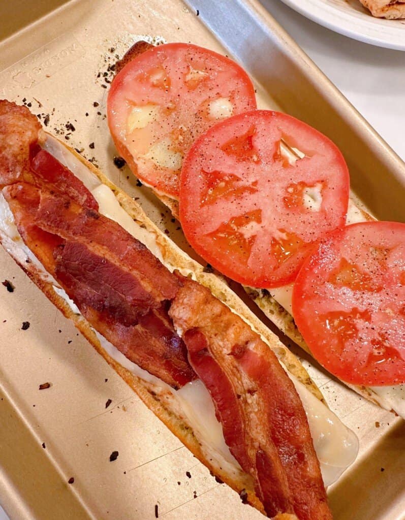 Adding bacon and tomato slices to sandwich.