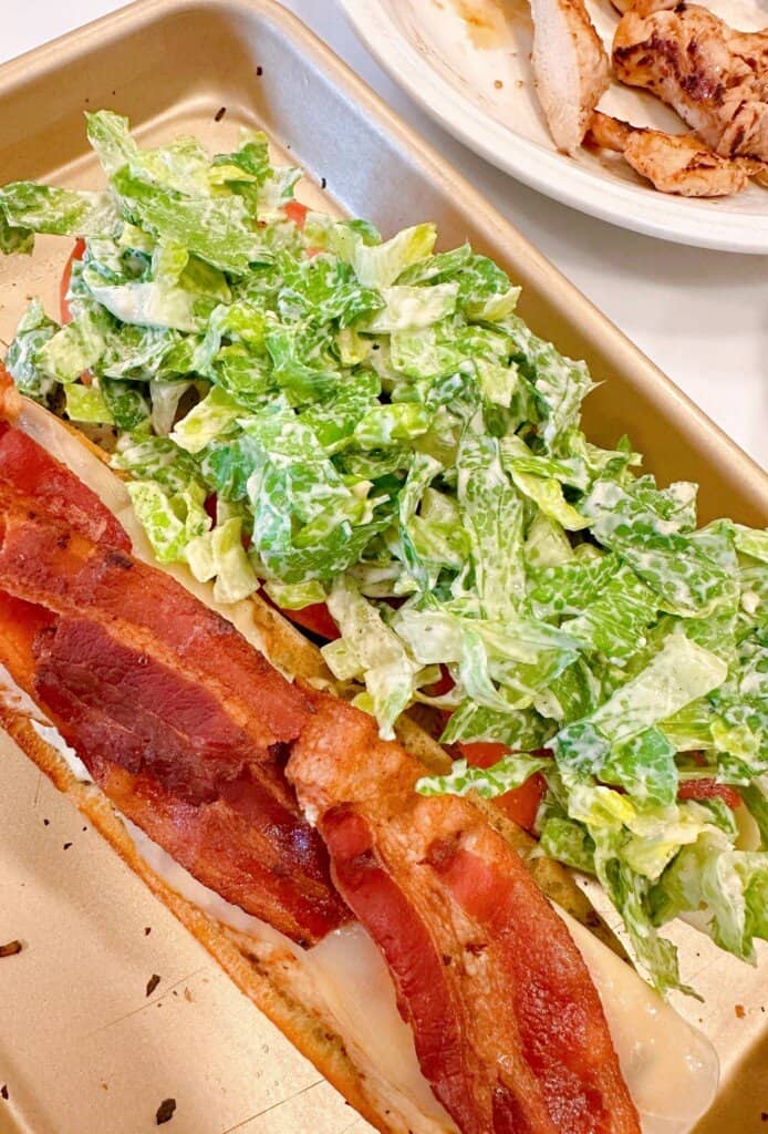 Adding tossed caesar salad to sandwich.