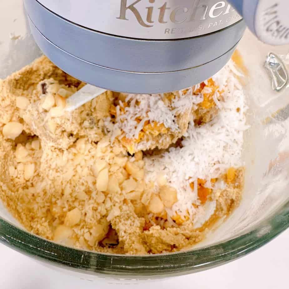 Adding coconut, mango, macadamia nuts, and chocolate chunks to dough.