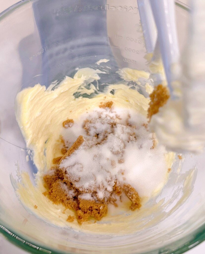 Adding brown sugar and white sugar to creamed butter in mixing bowl.