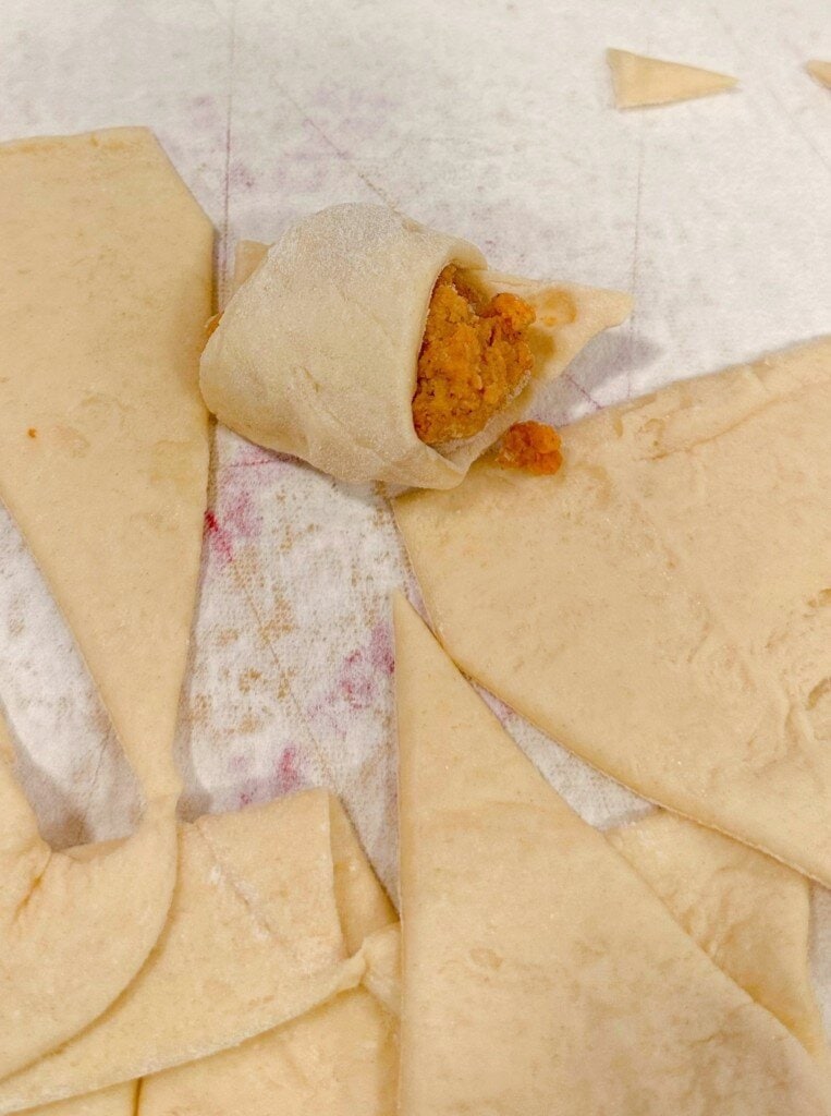 Wrapping chicken in cut crescent rolls.