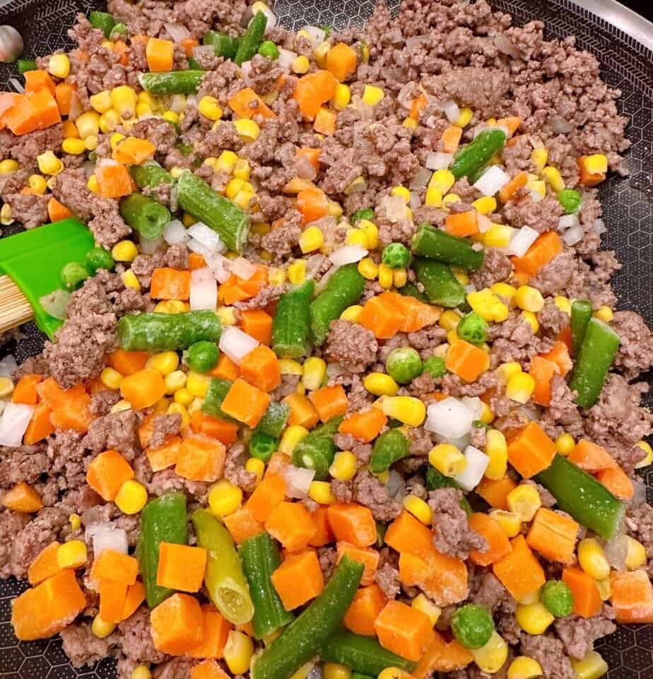 Adding frozen vegetables to ground beef mixture.