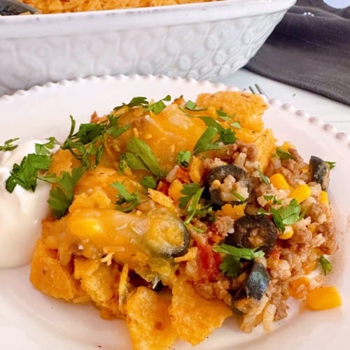 Cheesy Taco Rice Casserole serving on a white plate with cilantro and sour cream.