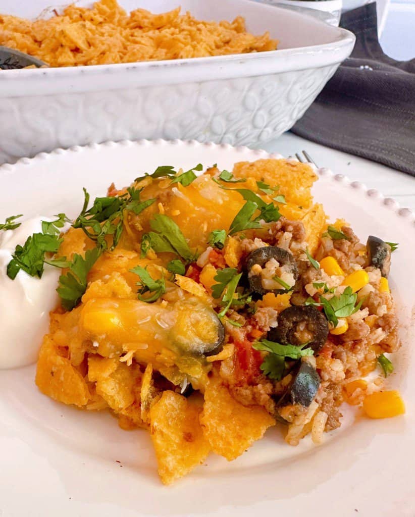 Cheesy Taco Rice Casserole serving on a white plate with cilantro and sour cream.