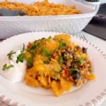 Cheesy Taco Rice Casserole with sour cream and cilantro with the full casserole in the back ground.