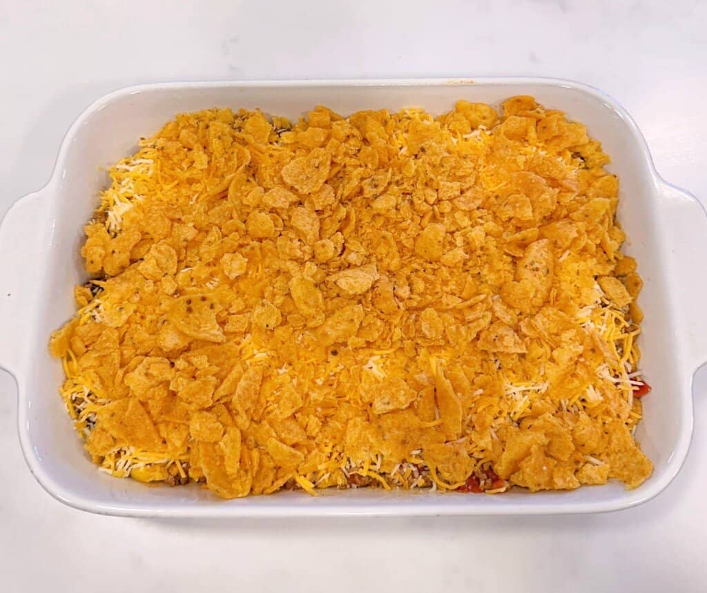 Finishing casserole with cheese and crushed corn chips.