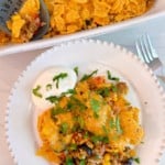 Cheesy Taco Rice Casserole with sour cream and chopped cilantro on a serving plate and in the casserole dish.