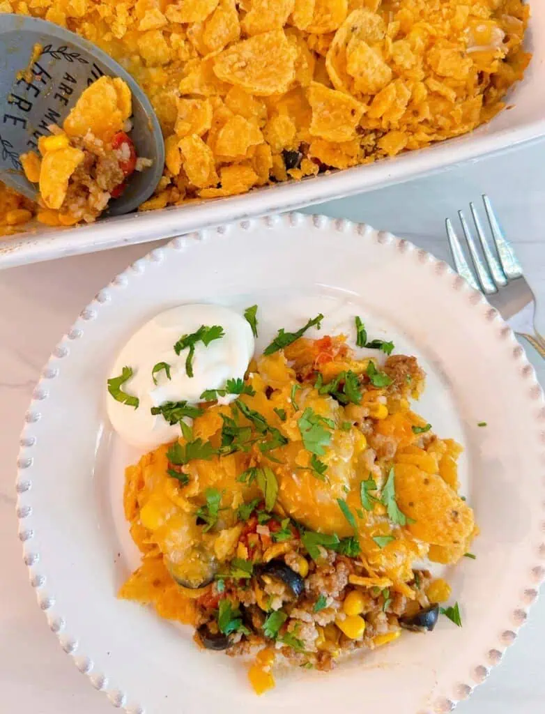 Cheesy Taco Rice Casserole with sour cream and chopped cilantro on a serving plate and in the casserole dish.
