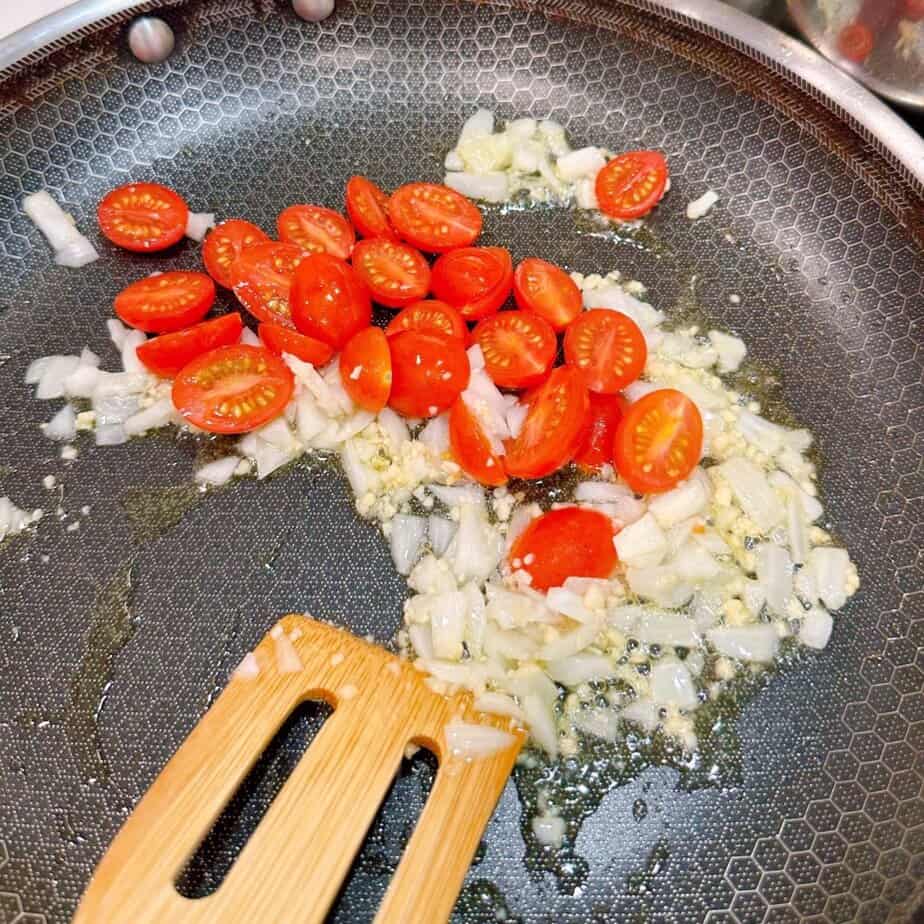 Adding cherry tomatoes to onions and garlic.
