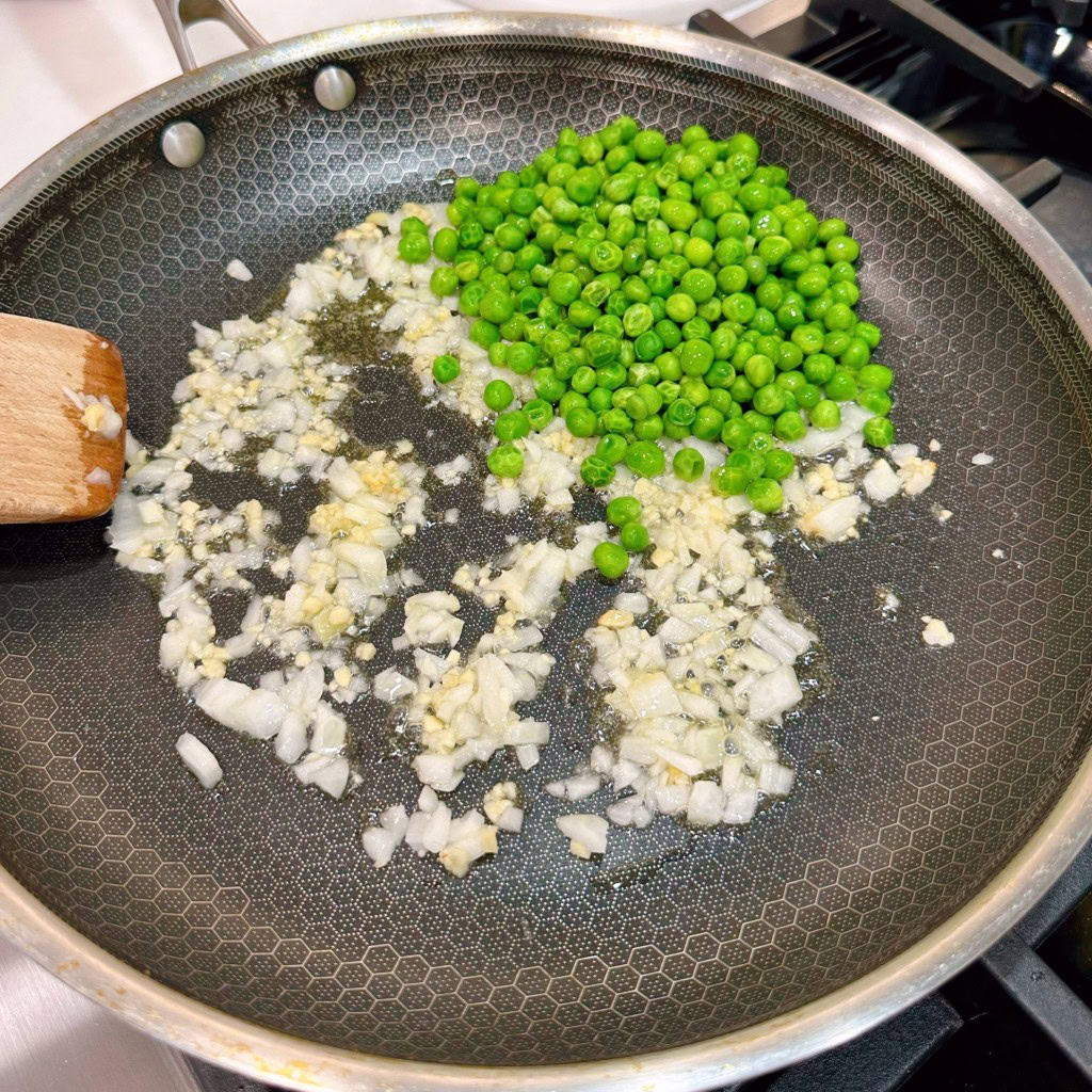 Adding peas to onions and garlic. Cooking over medium-high heat.