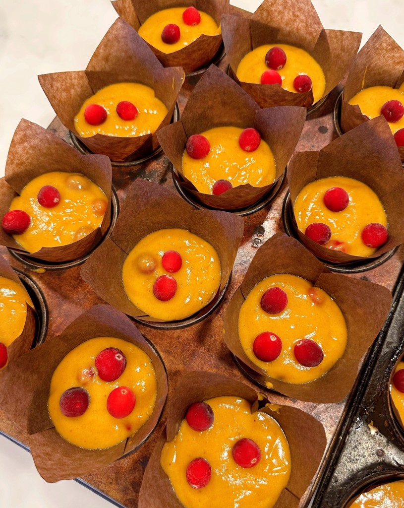 Filling muffin tins with cranberry pumpkin batter and adding extra cranberries on top.