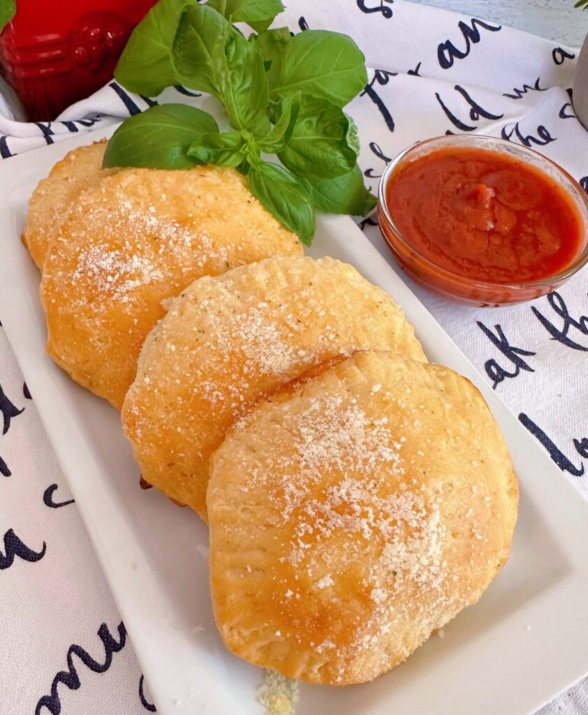 Pizza Pockets on a serving dish with a side of marinara sauce.