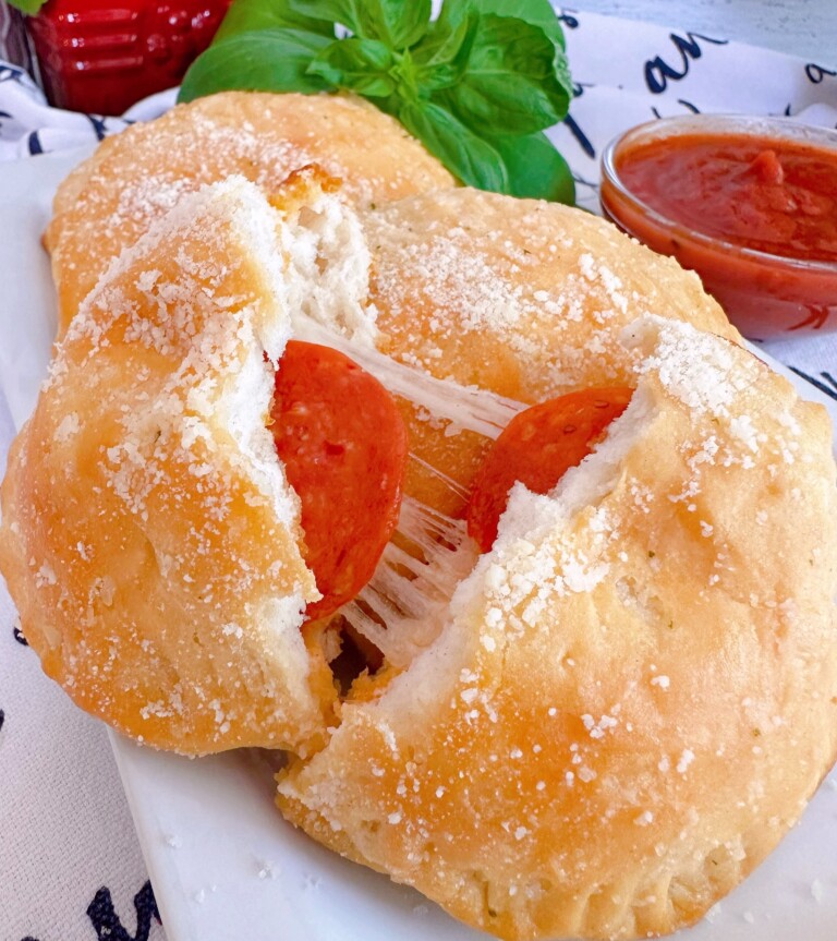 Biscuit Pizza Pockets on a plate with one broken open to reveal pepperoni and cheese.