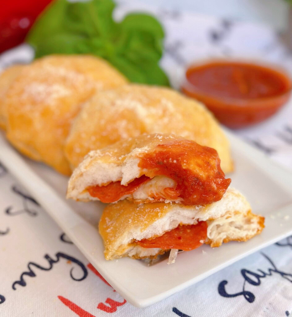 Pizza Biscuits torn in half with pizza sauce on the corner and a cup of pizza sauce near by.