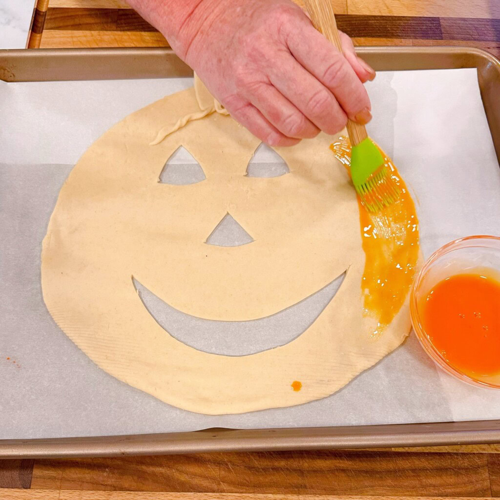Pie crust with jack-o'-lantern face cut out and the egg wash being brushed on.