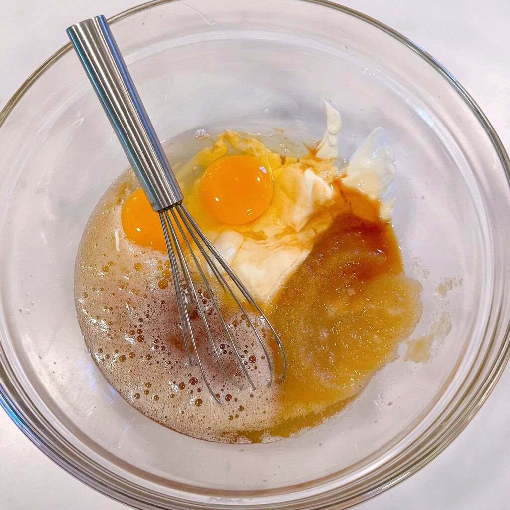 Cake wet ingredients in a bowl with a wire whisk.