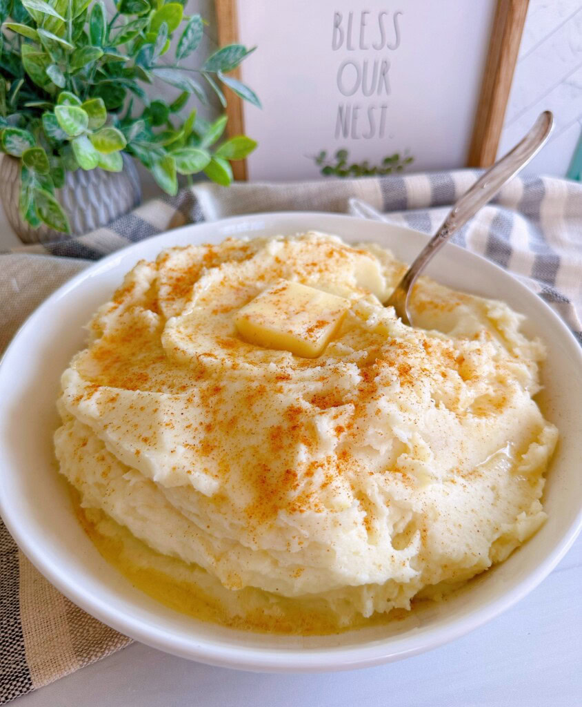 Homemade mashed potatoes in a large serving bowl with butter and a sprinkle of paprika.