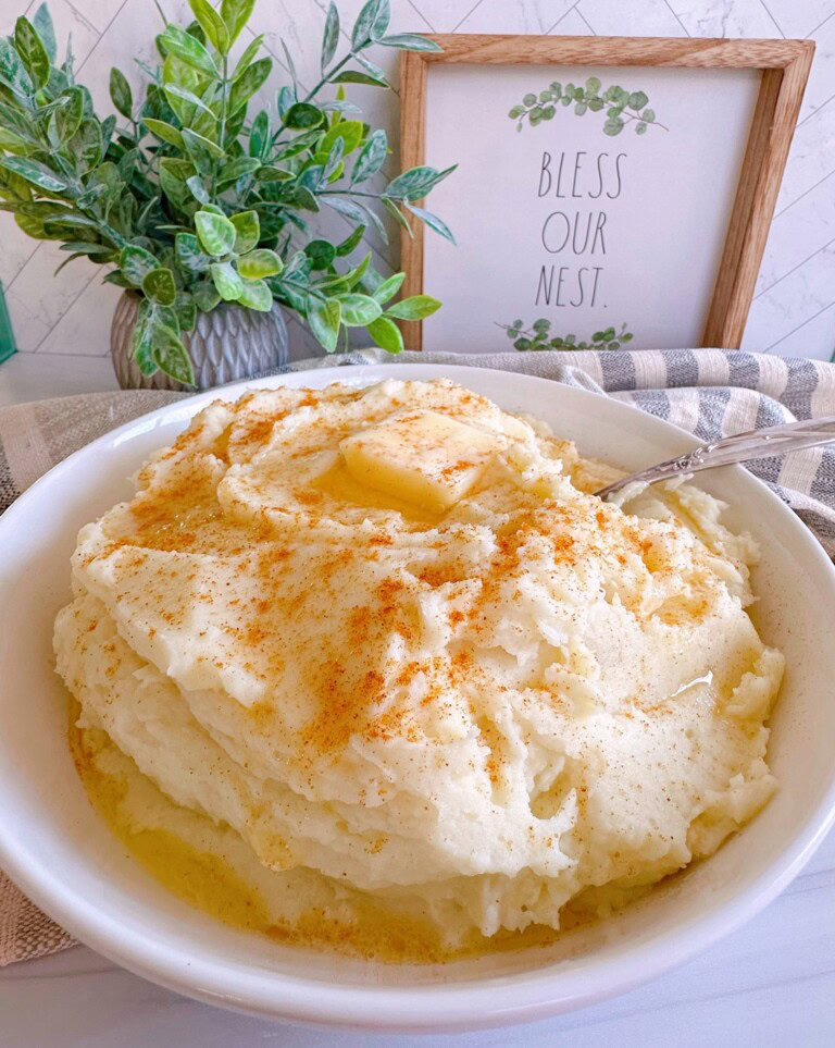 Mashed Potatoes in a large serving bowl with butter on top.